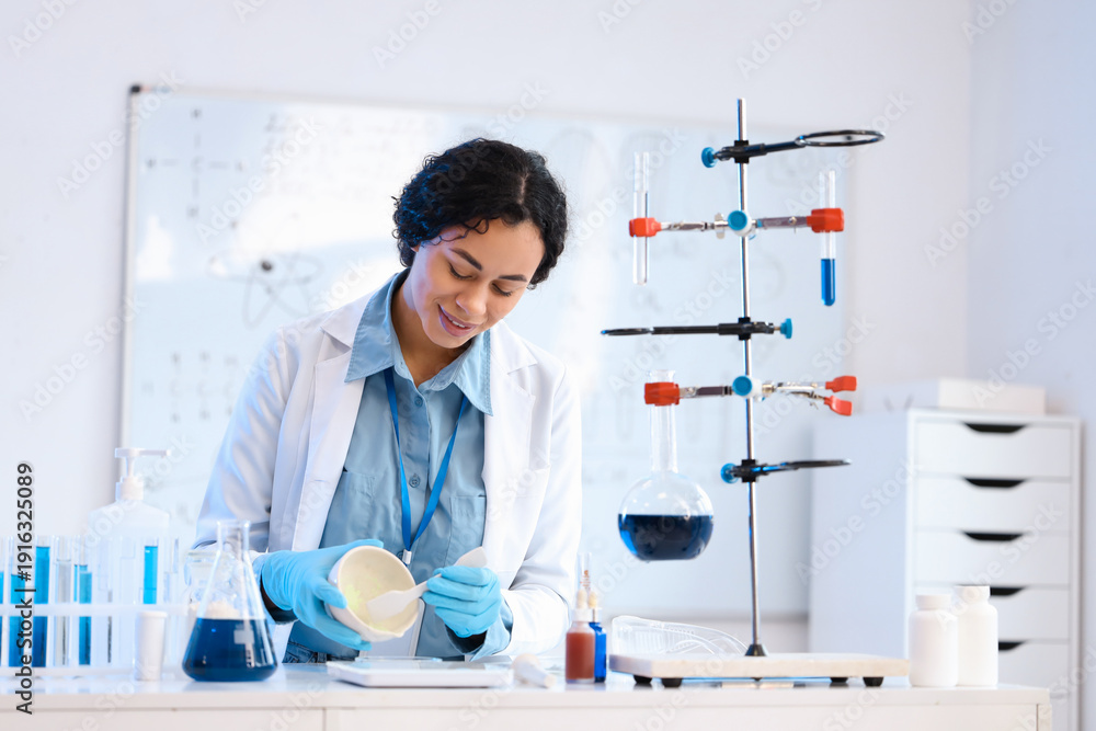 Fototapeta premium Pretty young African-American female chemist with mortar and Petri dish working in lab