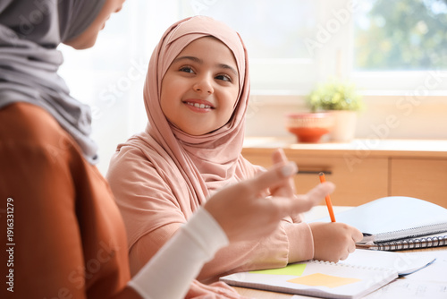 Little Muslim girl with her mother learning Arabic language at home, closeup