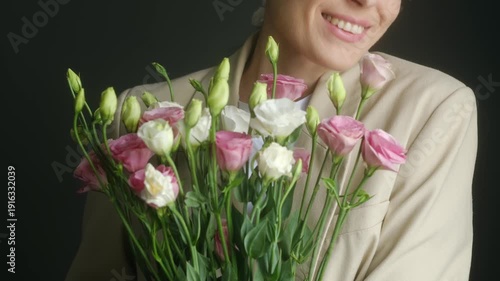 Joyful middle aged woman smelling beautiful bouquet pink, white eustoma flowers, smiling happily against dark background, representing special moment celebration, surprise. Woman and bouquet flowers.