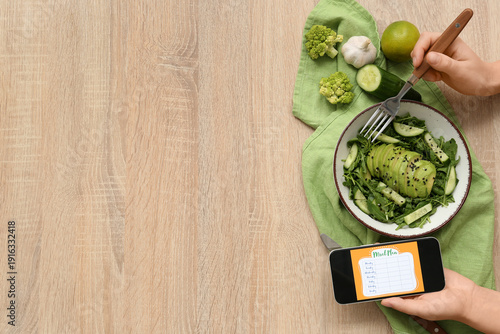 Slika na platnu Woman using mobile phone with meal plan and healthy food on brown wooden backgro