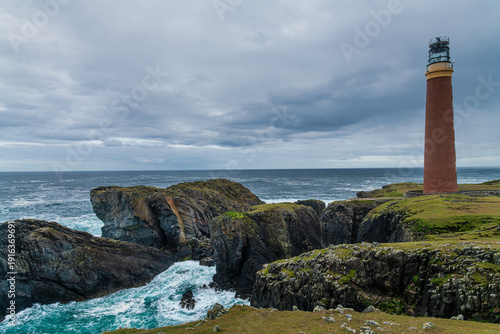 The 37 metre red brick tower of the Butt of Lewis Lighthouse over high sea cliffs at the most northerly point of the Isle of Lewis, Outer Hebrides, Scotland, UK