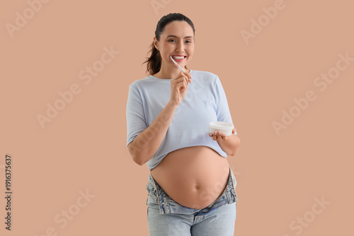 Pregnant woman brushing teeth on beige background