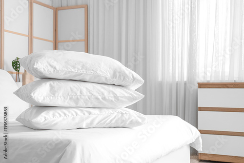 Cozy bed with white blanket and stack of soft pillows in stylish bedroom, closeup