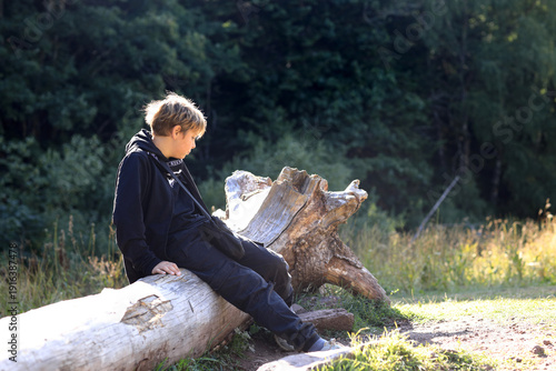 Boy resting on fallen tree trunk during hike