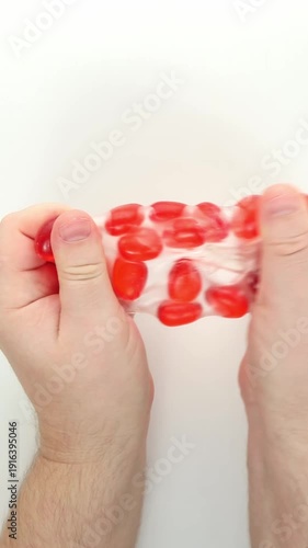 Two hands squeeze a red squish, sad, anti-stress, on a white background, the thumbs press deeper as the bubbles protrude then the grip relaxes and the toy regains its shape showing squeezing movements