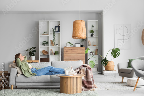 Young woman lying on grey sofa in light living room