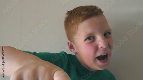 Adorable handsome baby rejoicing and pointing at camera. Portrait of happy red hair boy with freckles indoor. Close up emotions of male child with excited expression on face. Slow motion