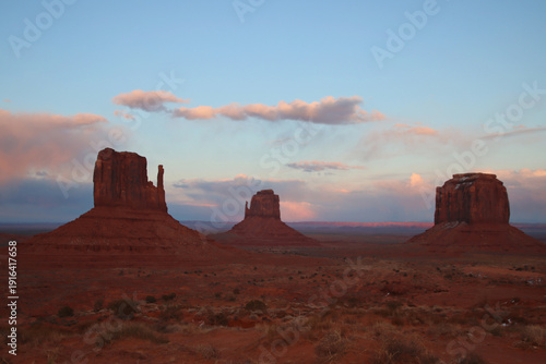 Sunset light illuminates the iconic sandstone buttes of Monument Valley, USA. East Mitten Butte, West Mitten Butte and Merrick Butte rise from the desert under a colorful evening sky.