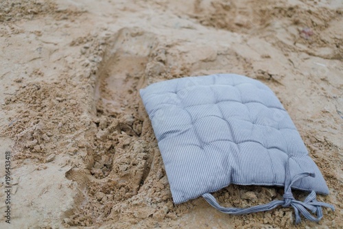 A cushion rests on sand, showing a footprint nearby in a dry outdoor space