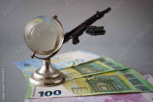 Wallpaper Mural Paper euro bills, a toy rifle and a small glass globe. Finance and economics. Armed conflicts. Torontodigital.ca