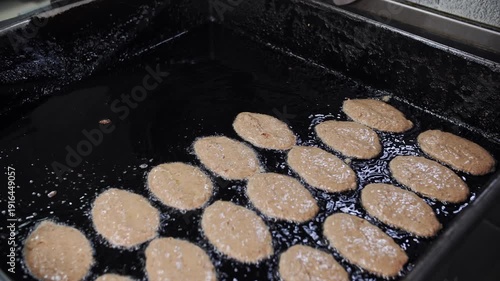 The cook puts the raw mass with a spoon in an iron plate of oil for cooking liver pancakes 