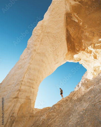 View of the stark white chalk cliffs frame a lone figure against the azure sky, creating a dramatic contrast of color and scale, Aktau, Mangystau Region, Kazakhstan.