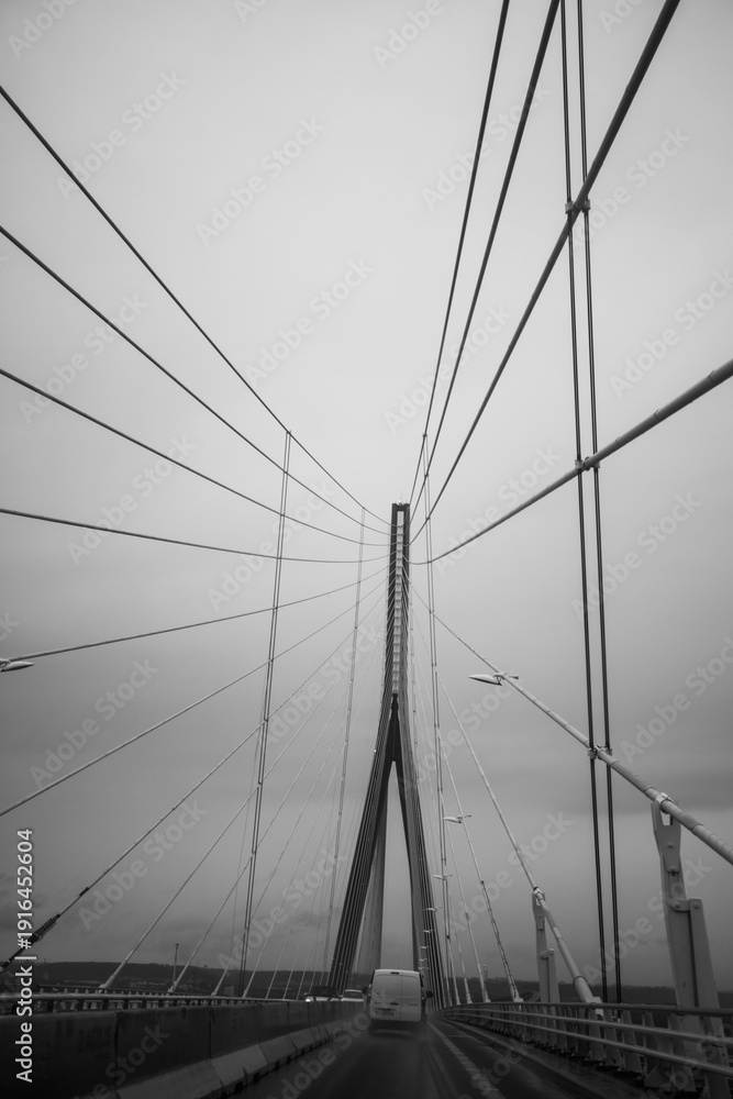 Fototapeta premium Monochrome view of a cable stayed bridge with vehicles on a wet road, dramatic architectural perspective and moody travel concept.
