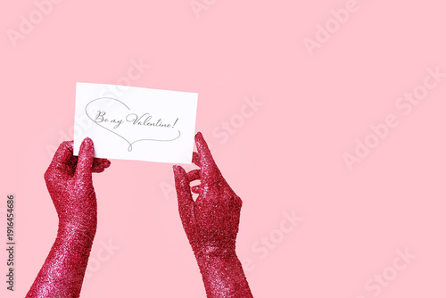 Painted female hands with greeting card for Valentine's Day celebration on pink background, closeup
