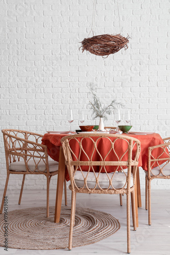 Autumn table setting with burning candles and dry leaves in light room