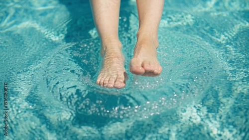 Bare feet of a person splashing water in a swimming pool, creating ripples and waves, showcasing the refreshing summer activity in a bright, sunny environment