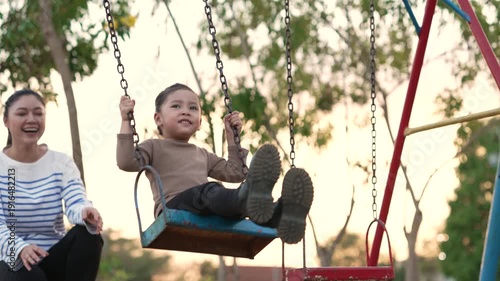 slow motion of cheerful child girl with mother playing on a swing at playground	