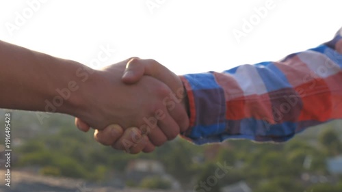 Close up of young men meeting on rooftop and greeting each other outdoor. Two friends shaking hands on cityscape background. Friendly handshake of guys. Concept of friendship. Dolly shot Slow motion