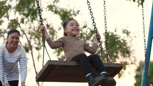 slow motion of cheerful child girl with mother playing on a swing at playground	