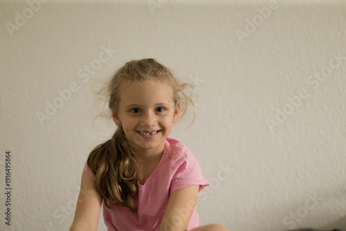 Photography Smiling girl in pink shirt sitting by wall, playful afterschool mood with tousle