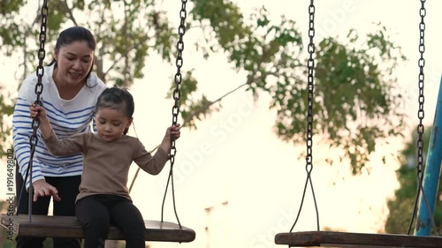 slow motion of cheerful child girl with mother playing on a swing at playground	