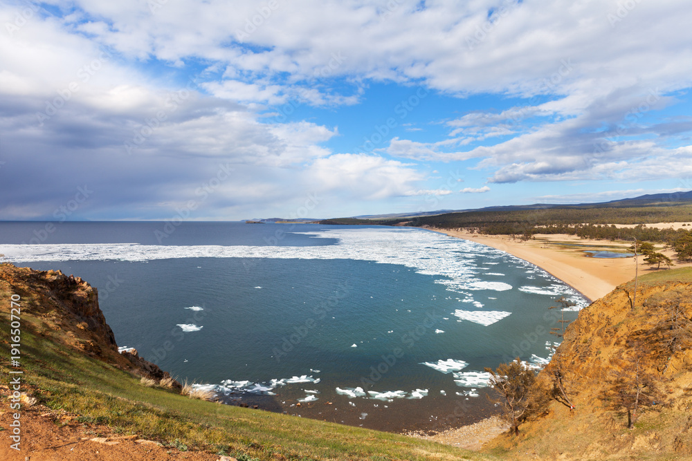 Obraz premium Baikal Lake in springtime. View of the sandy beach of the Sarayskiy bay with melting ice near near the village of Khuzhir. Beautiful spring landscape. Natural background. Spring travels and outdoors