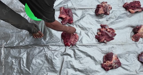 Person arranging raw meat pieces on a silver tarp.
