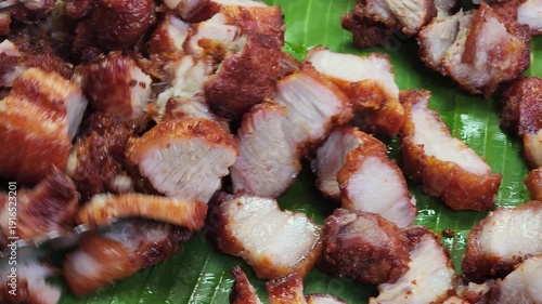 Street food vendor slicing crispy pork belly on a wooden chopping block, showing crunchy skin and juicy meat during traditional Asian food preparation.