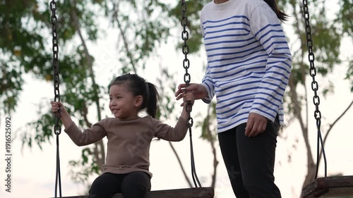 slow motion of cheerful child girl with mother playing on a swing at playground	