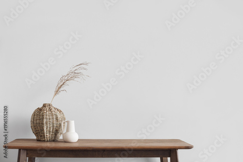 Minimal Scandi interior over white wall with empty blank space. Wooden table and vase. Soft natural light, calm cozy atmosphere. Empty gray wall background