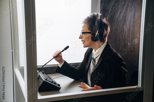 Bild auf Leinwand Female interpreter wearing headset speaks into microphone inside soundproof boot