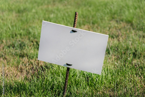 Blank white signboard on rusty metal stake in green grass.