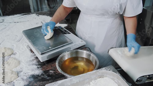 Professional baker weighing raw dough pieces on electronic scales in industrial bakery