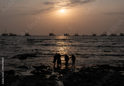 Sunset on the sea in Mumbai, India. In the background, cranes working on the construction of a new bridge,
