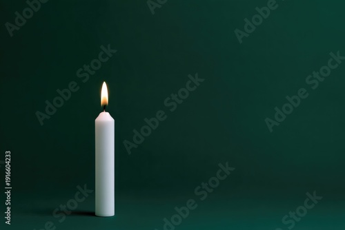 White candle emits warm glow against deep green backdrop, creati