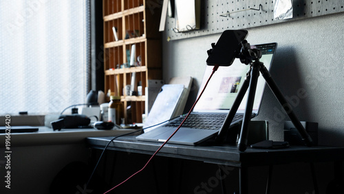 Foto リモートワークのデスク風景 ノートパソコンと三脚に固定されたスマートフォン ライブ配信 / Remote work desk setup with laptop