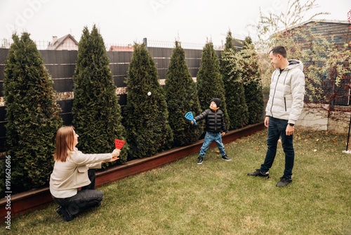 Obraz na plátne Young family playing velcro catch ball game together in their green backyard sur