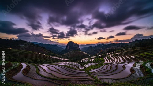 Time-lapse of the sun setting over scenic terraced rice fields reflecting the colorful sunset and starry night sky