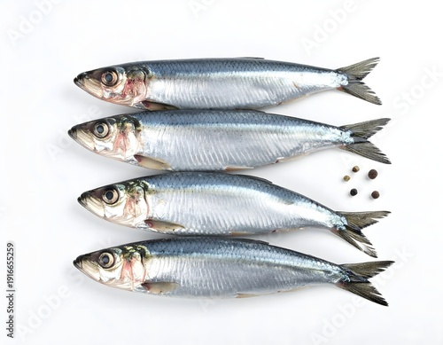 Four fresh whole sardines with vibrant silver scales arranged horizontally on a white background, accompanied by a sprinkle of black peppercorns, ready for seasoning.