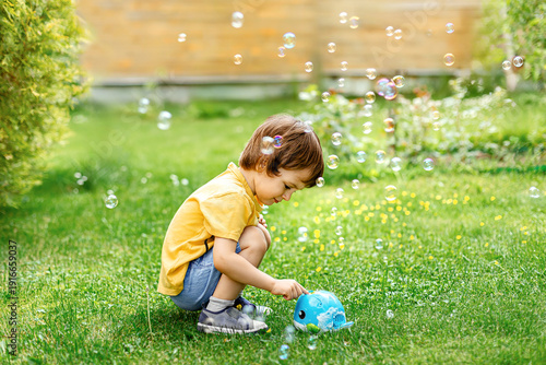 Cute toddler playing with bubble machine on green lawn, happy childhood outdoors.