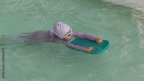 slow motion of preschool child girl learning to swim with board in swimming pool