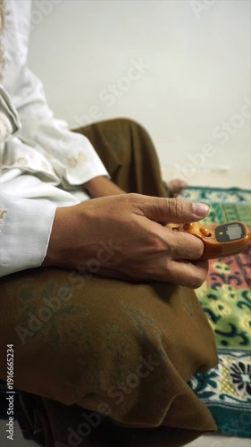 a Muslim is reciting dhikr while sitting using a digital prayer bead on a white background