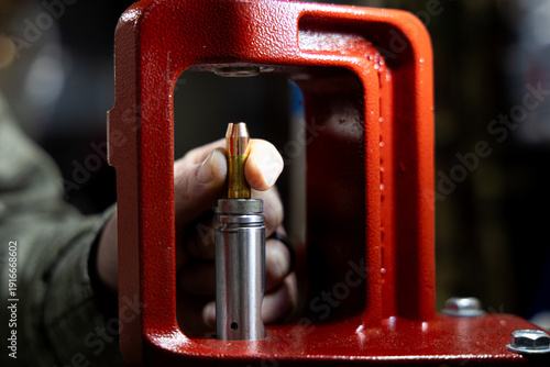 Quadro su tela Close-up of a hand placing a bullet into a reloading press for ammunition manufa