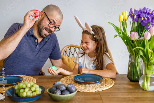 Father and daughter playing tapping game with colorful easter eggs at a festive dining table representing family bonding and holiday joy