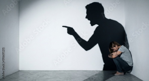 Woman crouching defensively as threatening male shadow looms overhead depicting verbal abuse and domestic violence concept
