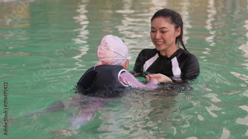 slow motion of preschool child girl in life jacket learning to diving with her mother in swimming pool