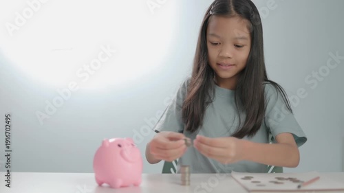 collections video Asian kid girl count and putting coin into pink piggy bank. Concept of financial literacy for kids, saving money for future education, investment planning, Isolated light background.