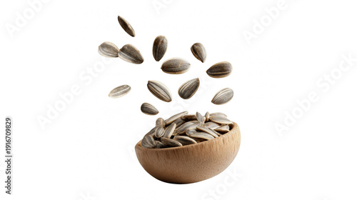 Sunflower seeds falling into a small wooden bowl isolated on a white background