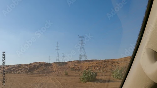 Point of view from SUV driving across wide desert dunes under strong sunlight with vehicle hood visible, natural lighting outdoors, concept of off road adventure and exploration.