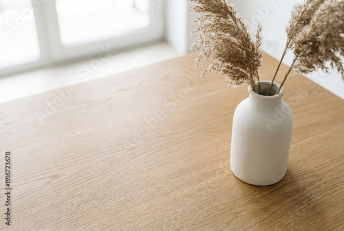 Minimalist wooden table with dry plant vase. Clean Scandinavian interior background with copy space for lifestyle or home decoration text.
